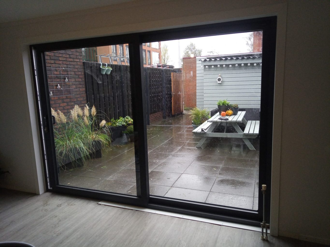 schuifpui Uitzicht op een betegelde achtertuin met planten en een houten tafel.