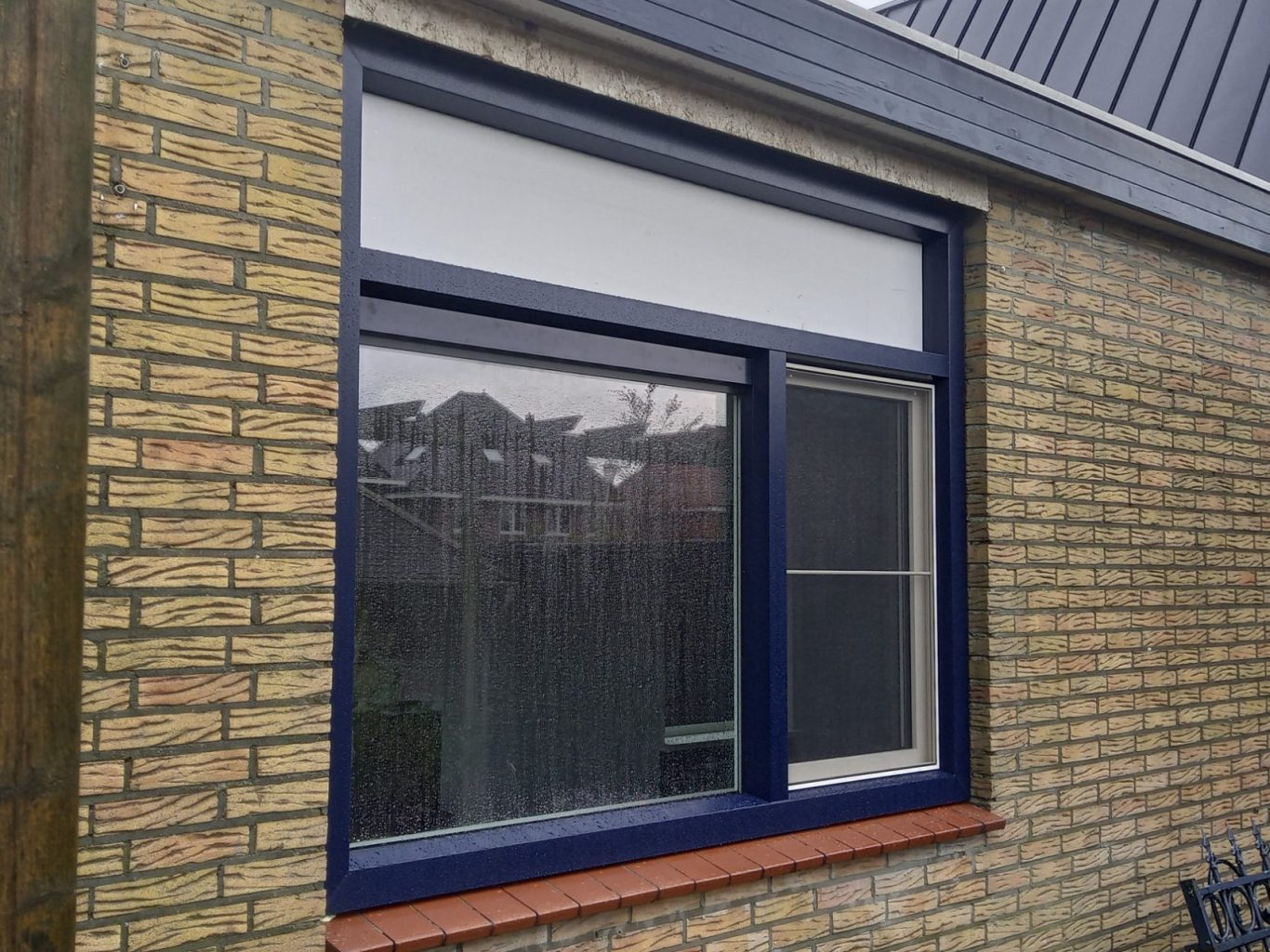 kunststof kozijn Blauwe raam omgeven door een stenen muur met een witte bovenpaneel.