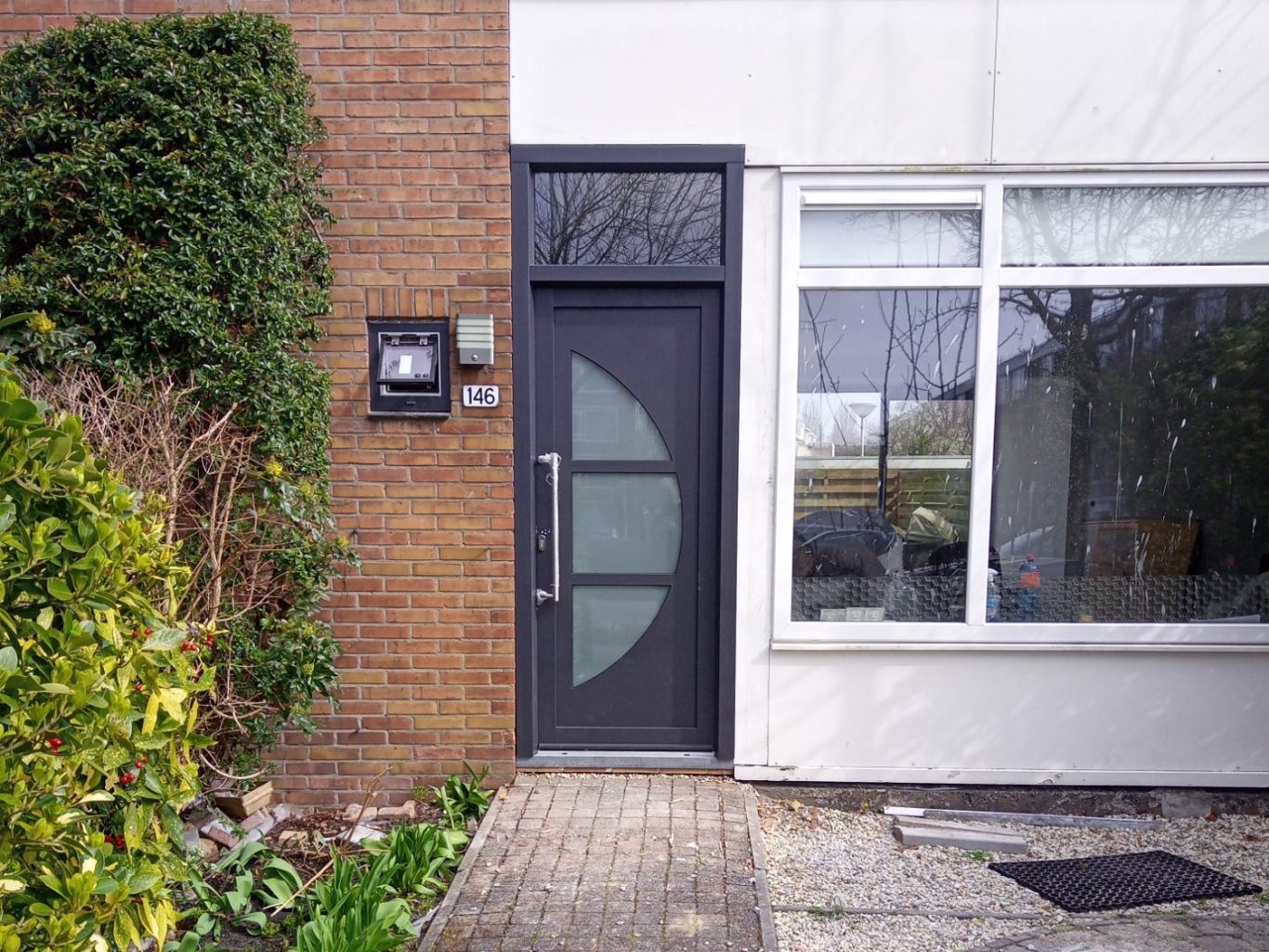 deur Zwarte deur met ronde glazen elementen naast een lichtbruine bakstenen muur.